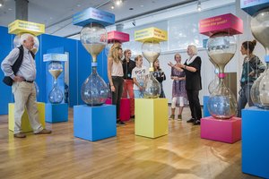 Photo of large sand clocks in the entrance area of the Dialogue with Time exhibitions. the sand clocks are titled with various questions, like: "What does best age mean?", "Would I like to turn the time ahead?"