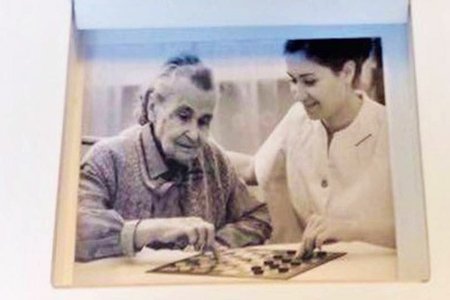 Foto, das eine alte Frau mit einer Pflegerin zeigt, die Dame spielen.