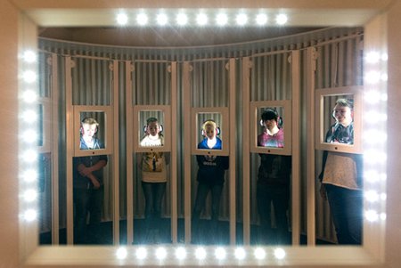 Bild einer Besuchergruppe im Raum "Galerie der Gesichter", wo jeder Teilnehmer hinter einem beleuchteten Rahmen Platz nimmt.