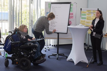 Foto von drei Frauen, die einen Workshop leiten. Eine der Frauen ist blind und eine sitzt in einem Rollstuhl.