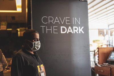 Photo of a guide standing next to a wall on which a writing says "Crave in the Dark"