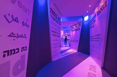 Photo of the "Tunnel of Questions" in the Dialogue with Time exhibition Holon, Israel. The walls of the tunnel are bathed in purple light and various questions around the topic of age are written on them.